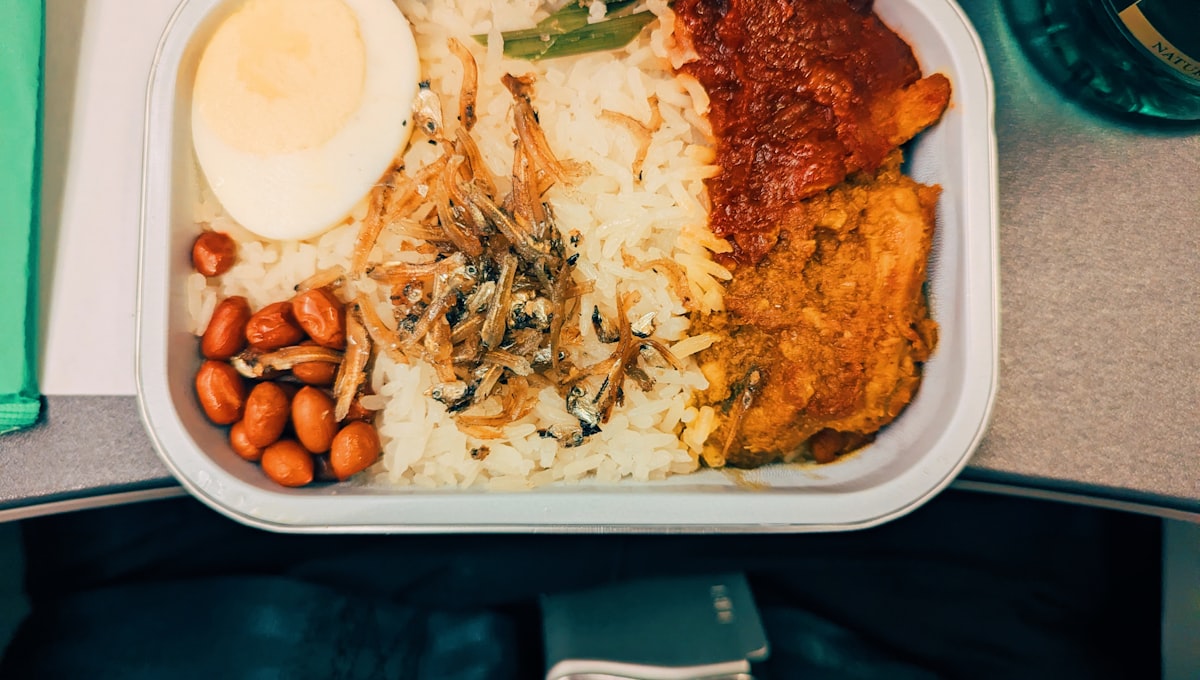 Flight attendant serving meal to passenger in premium economy cabin with white tablecloth service